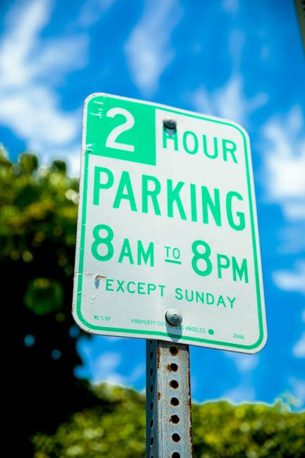 A circular street parking restriction sign with a red border, blue background, and a red slash indicating no parking, mounted on a metal post casting a shadow on a textured brick wall made of cream, g
